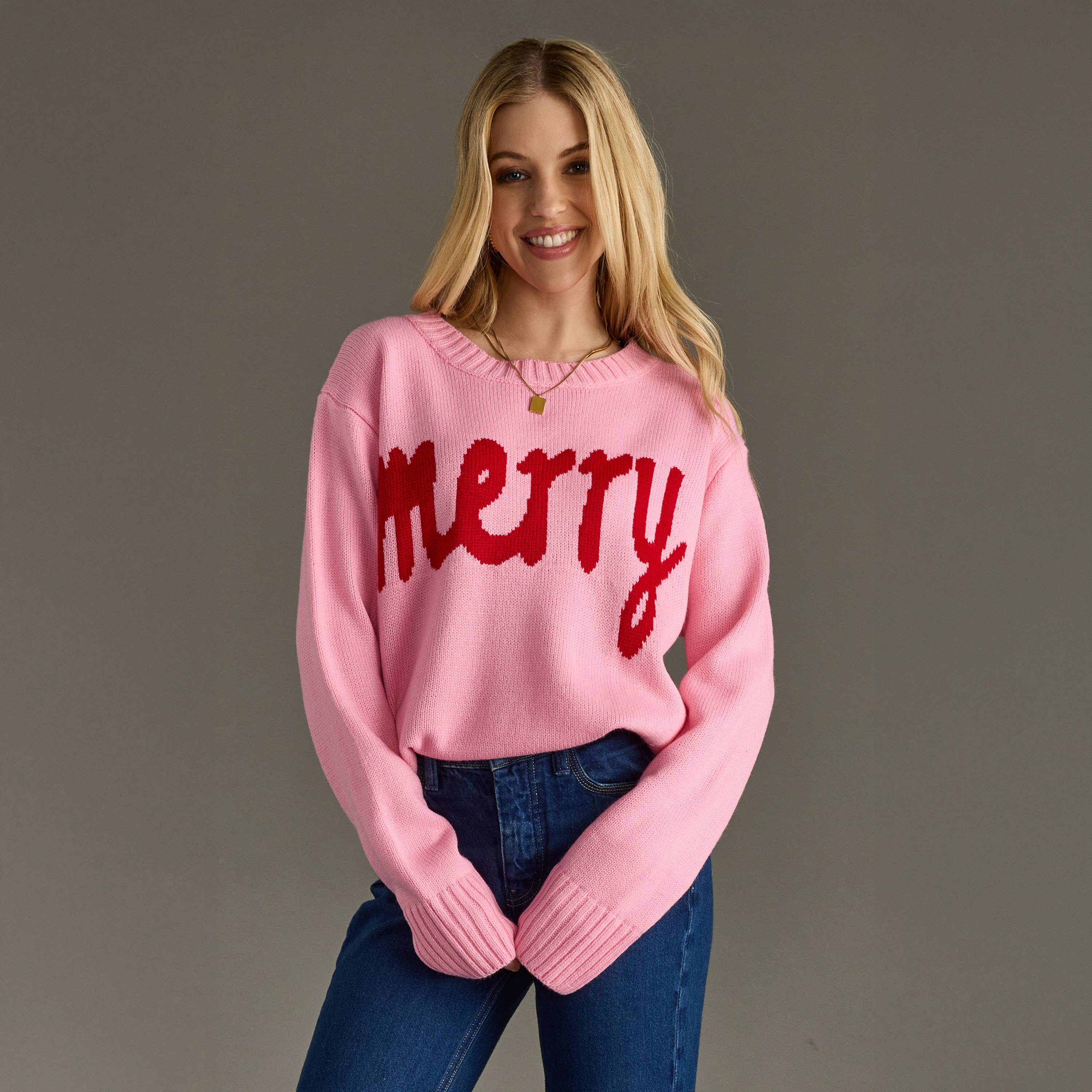 Woman wearing a pink sweater with 'merry' in red text against a gray background
