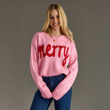 Woman wearing a pink sweater with 'merry' in red text against a gray background